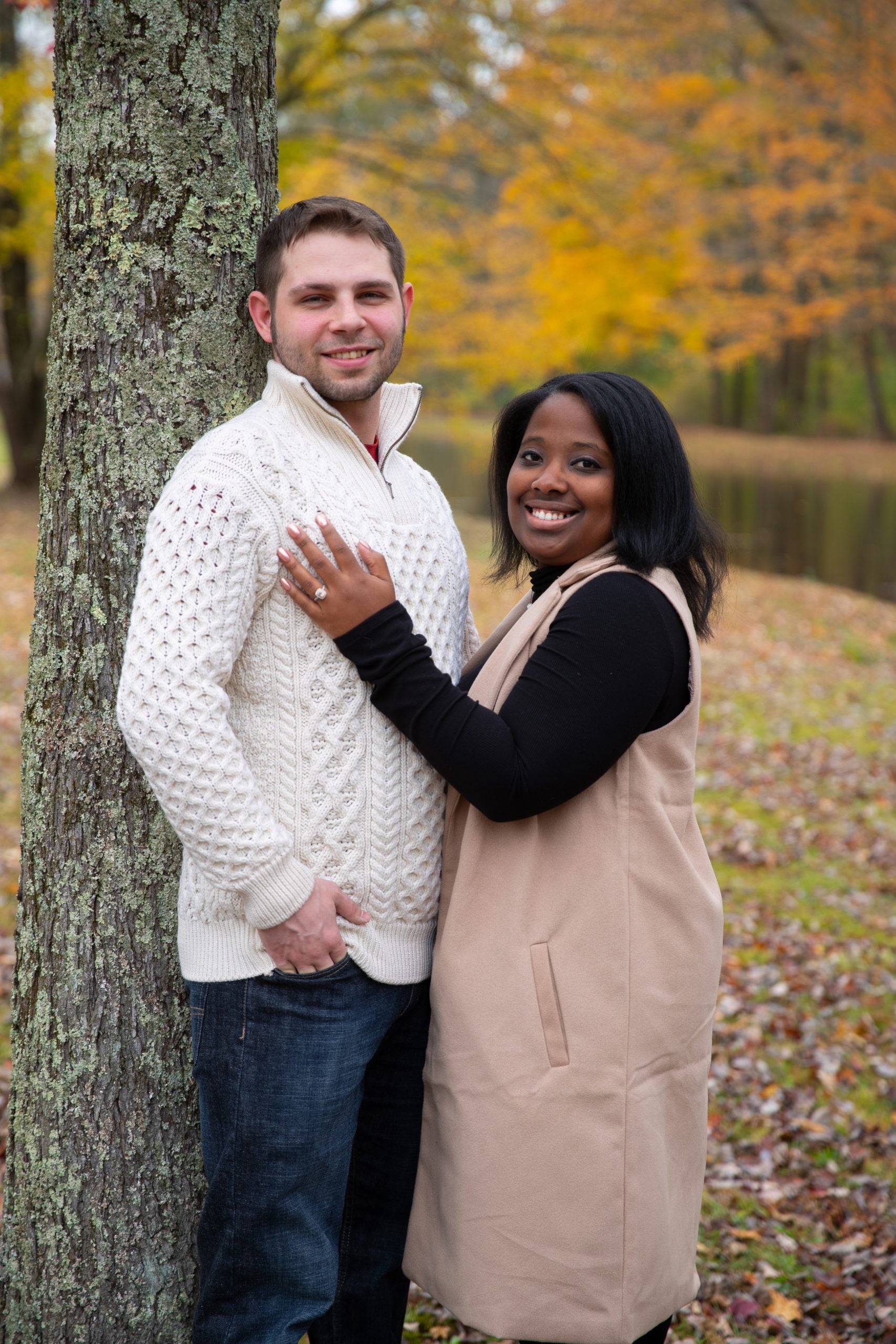 A man and woman are posing in front of a tree.