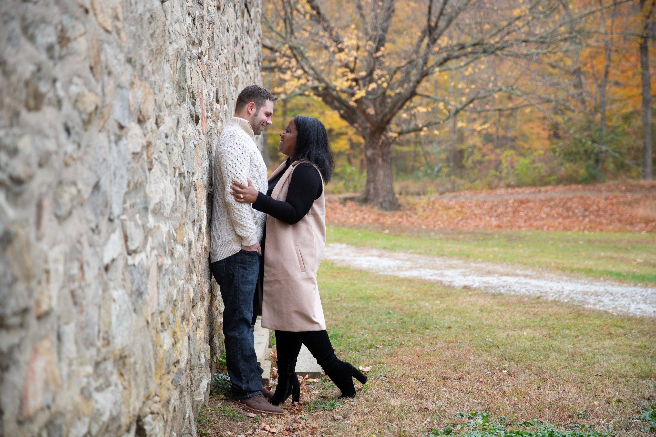 An engaged couple leaning against a stone wall.