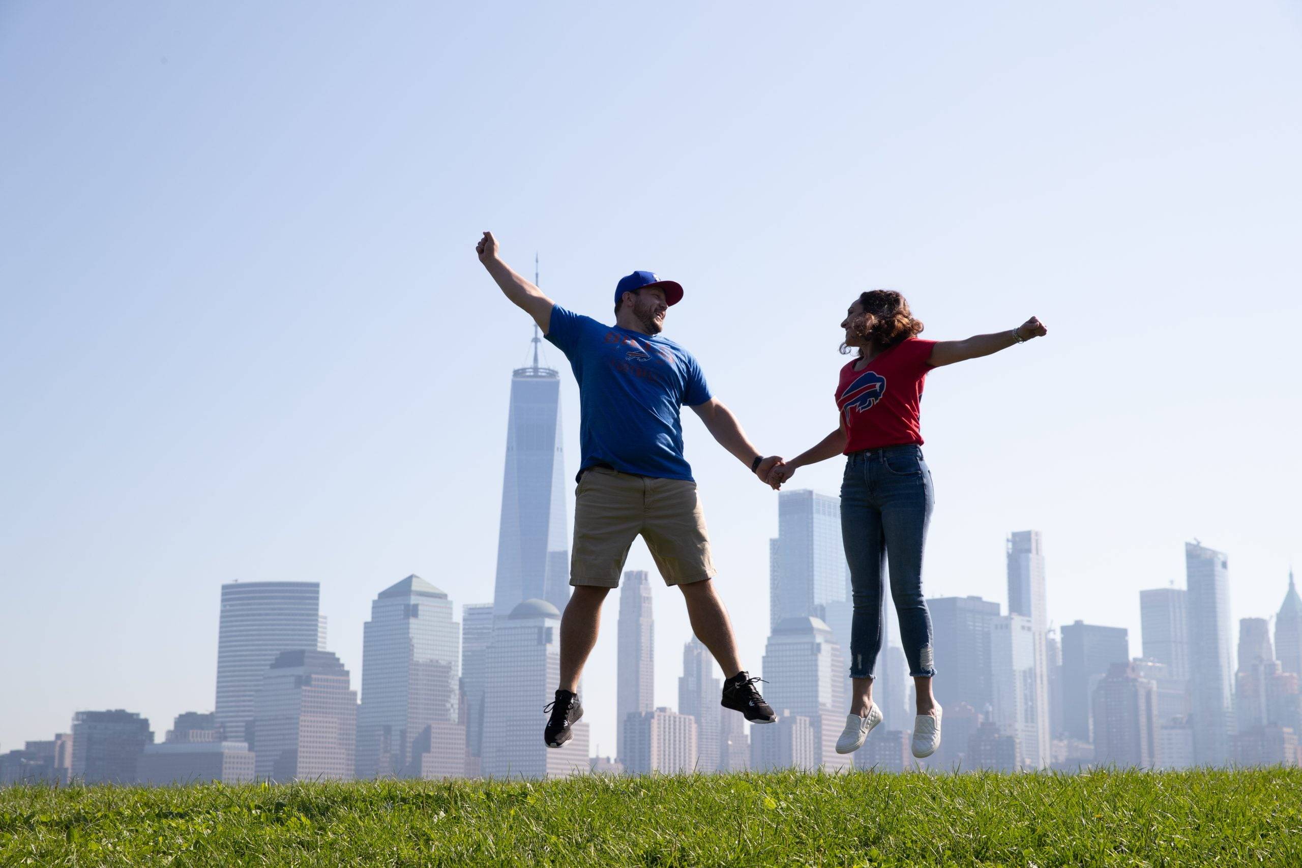 A couple jumping in the air with a city skyline in the background.