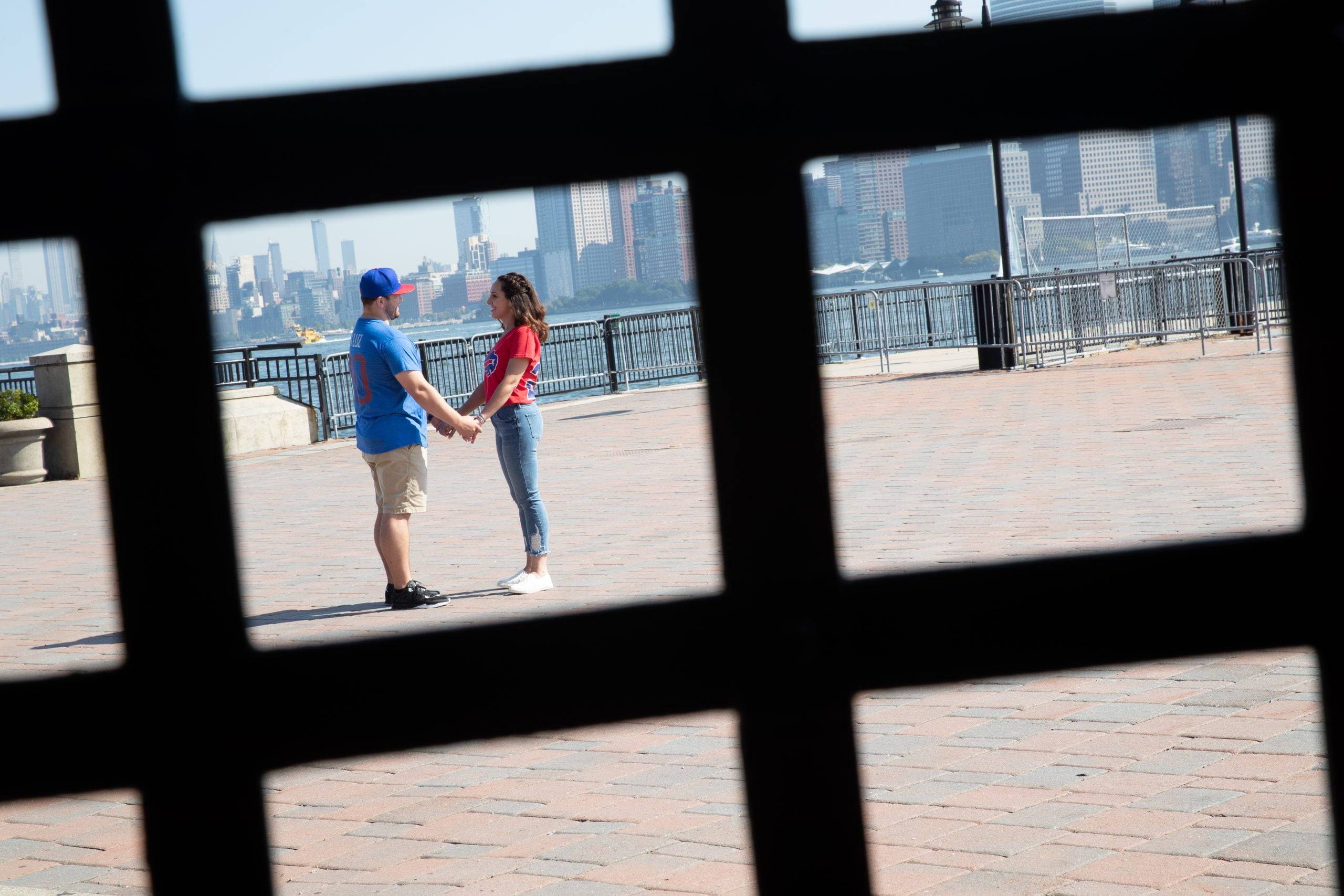 A couple holding hands through a fence in front of a city skyline.