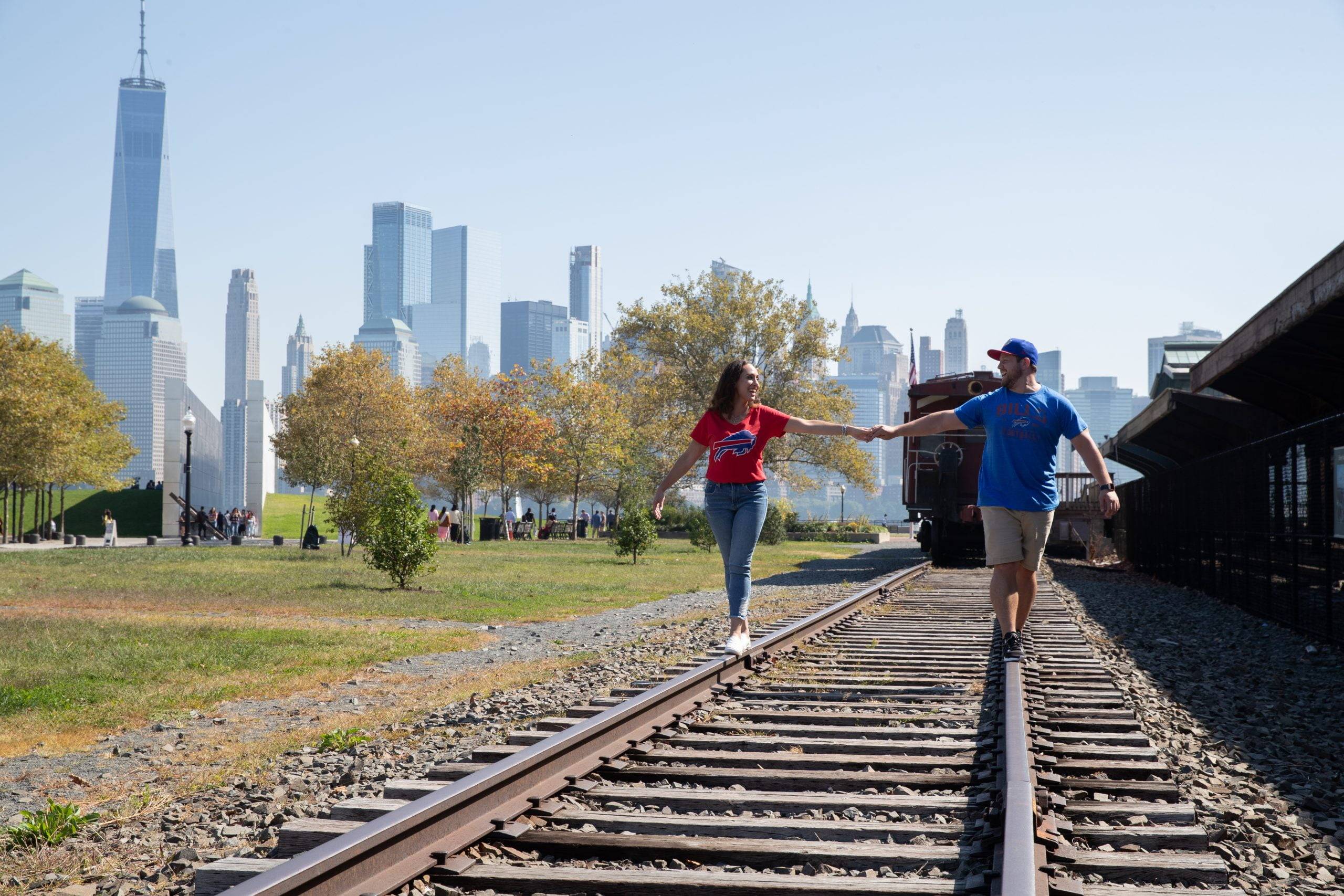 A couple walking on railroad tracks with a city skyline in the background.