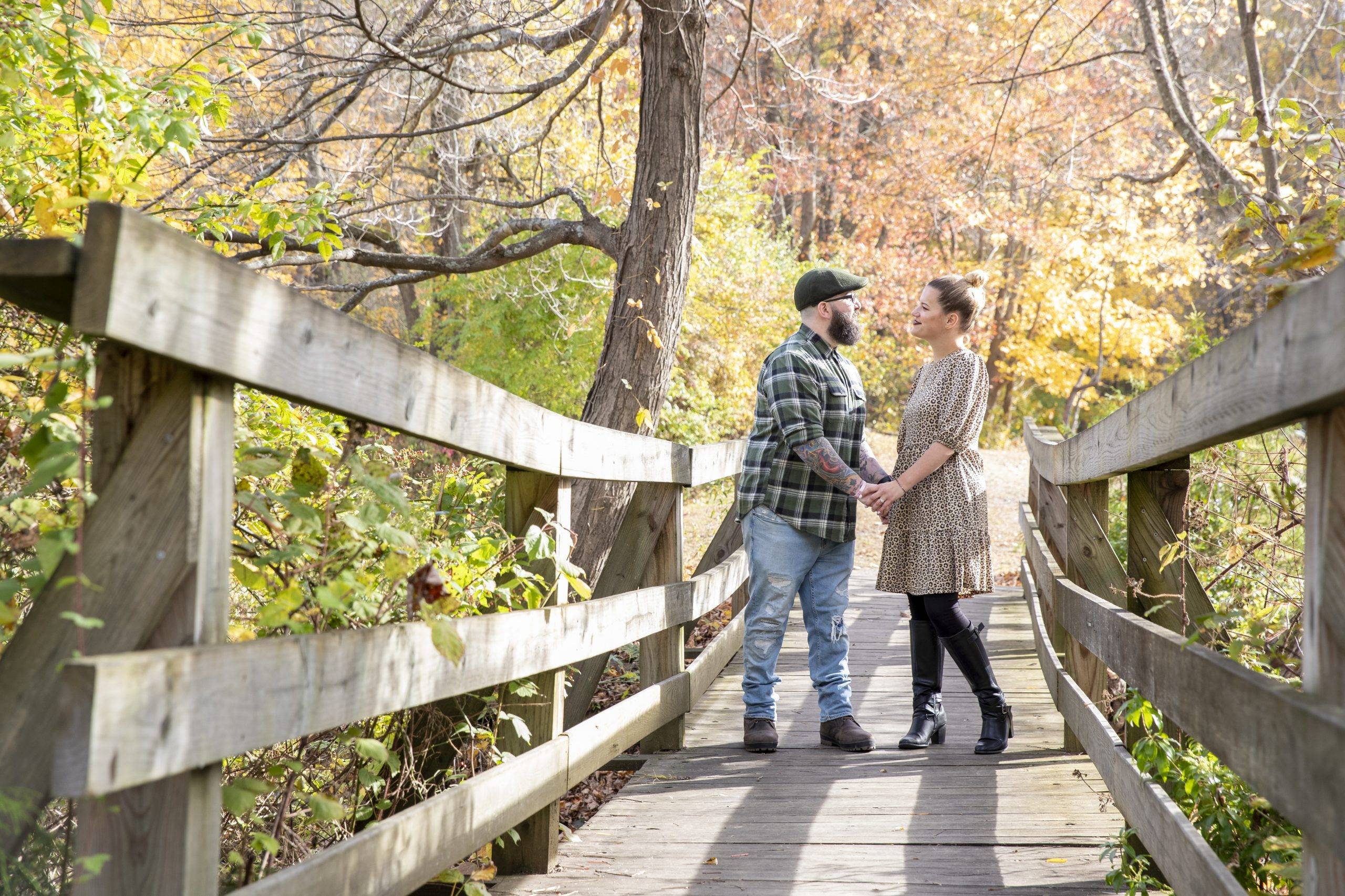 An engaged couple standing on a wooden bridge in the fall.