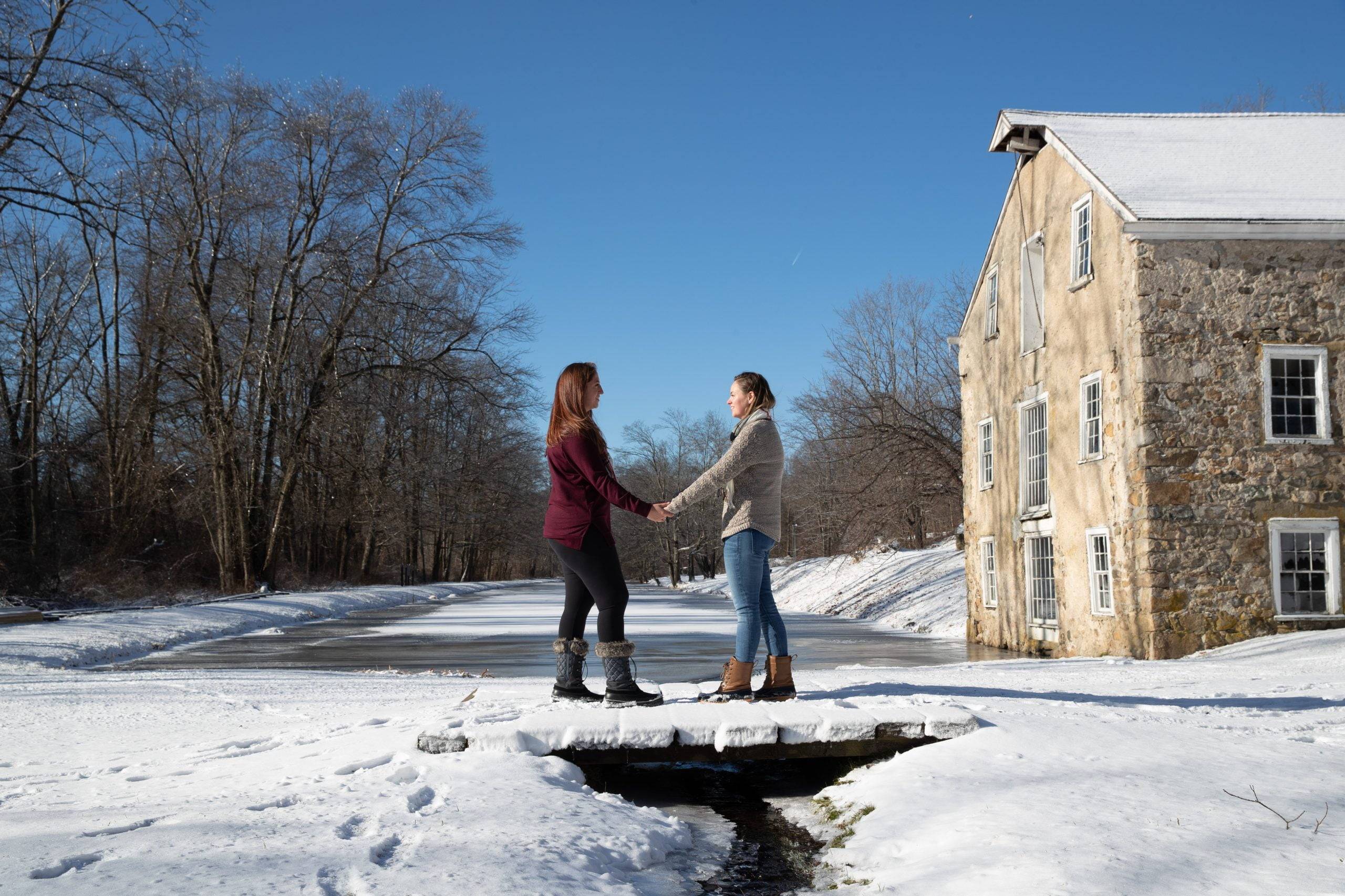 Two people standing on a bridge near a stone building in the snow.