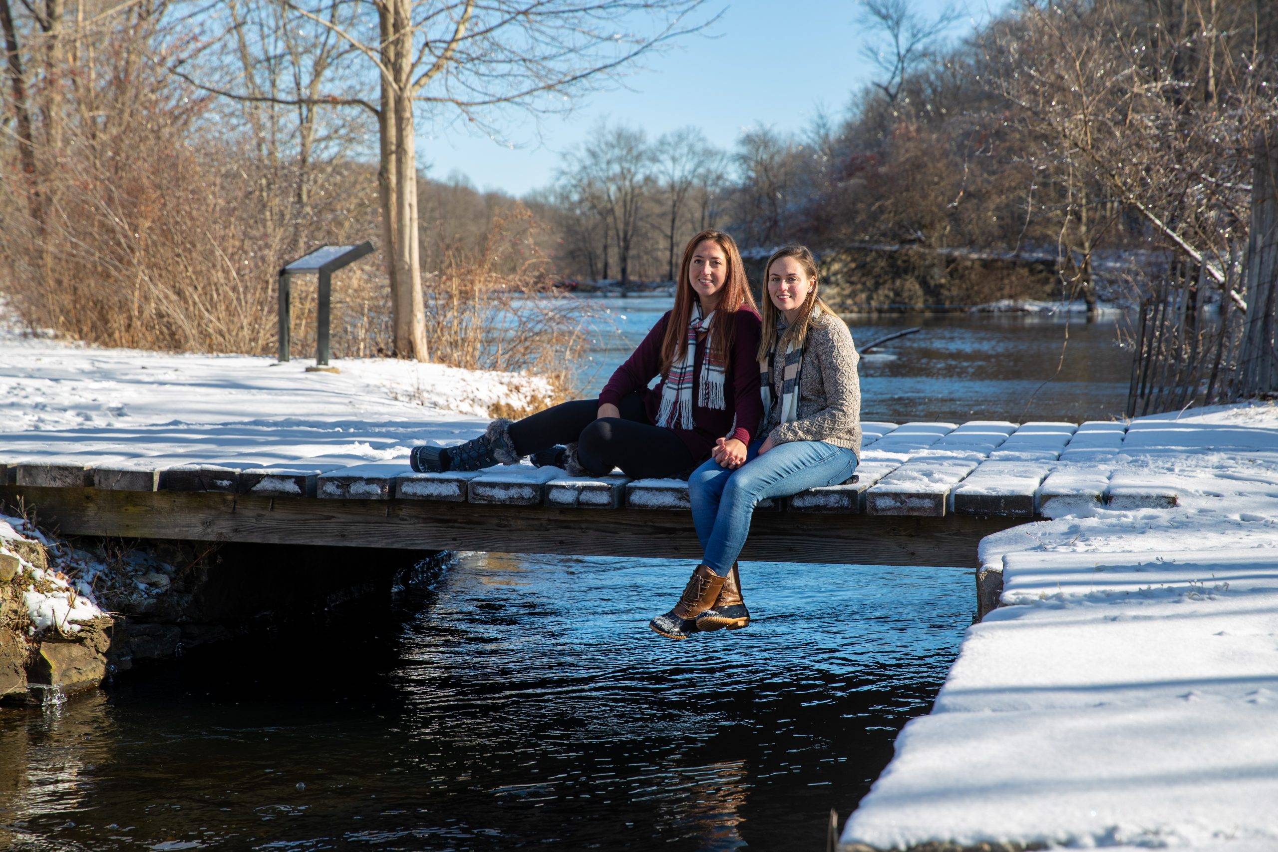 Two girls sitting on a wooden bridge in the snow.