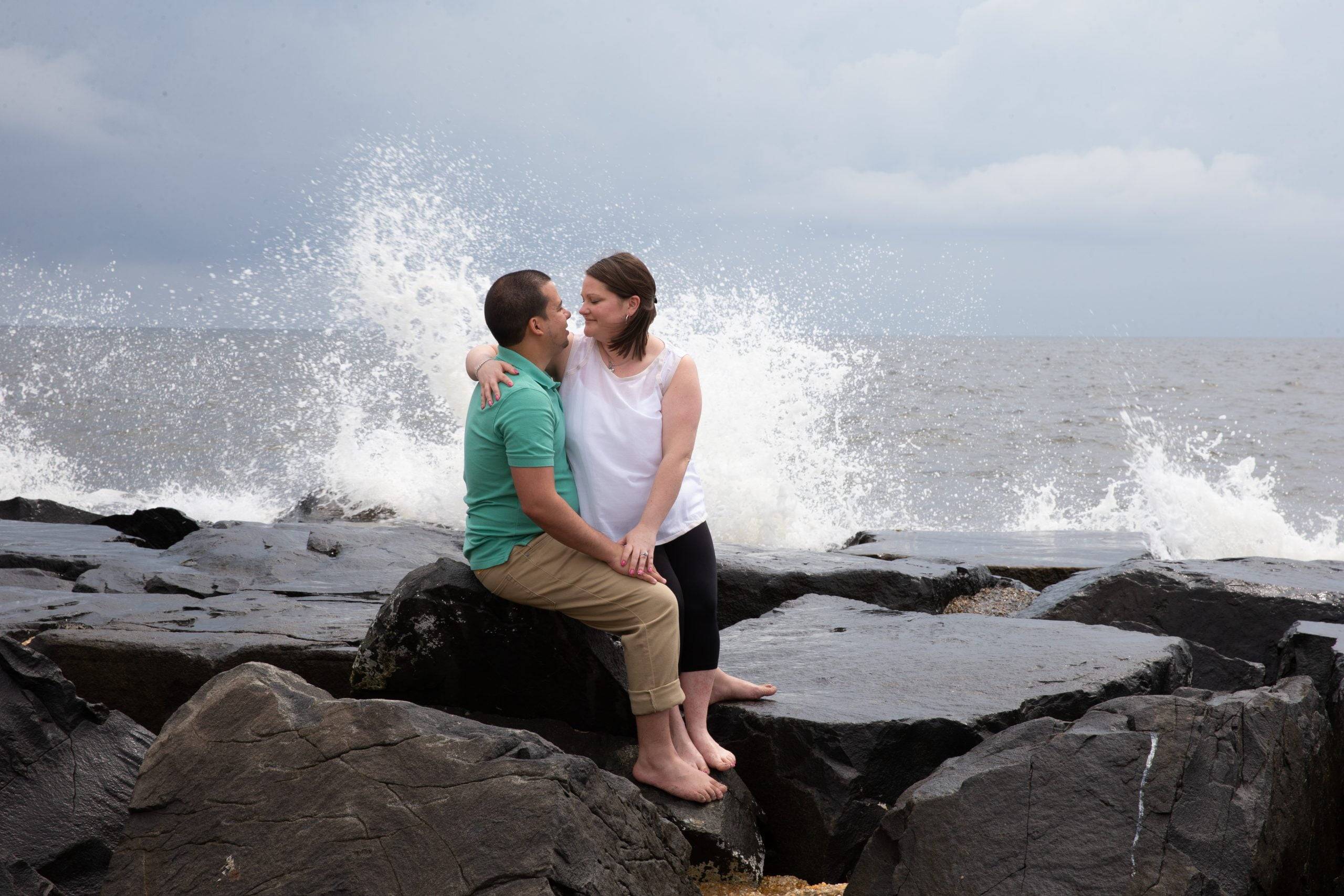 A couple sitting on rocks in front of the ocean.