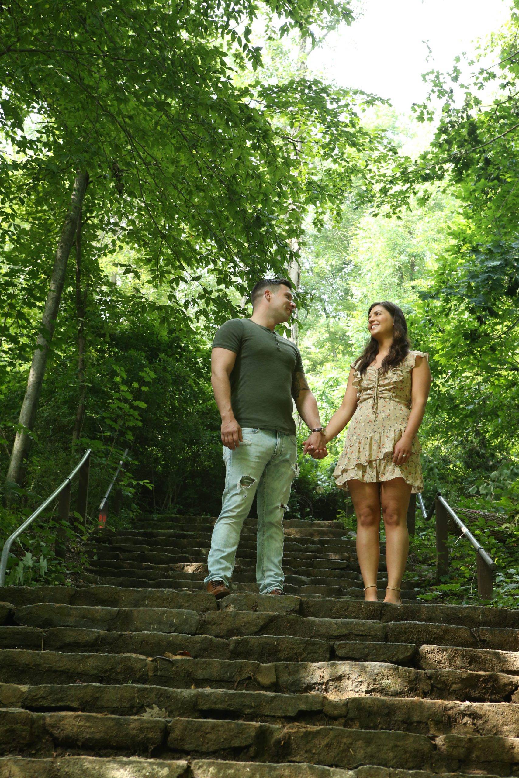 A couple standing on the steps of a wooded area.
