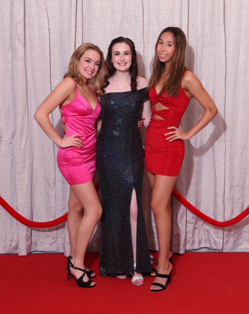 Three women posing on a red carpet.