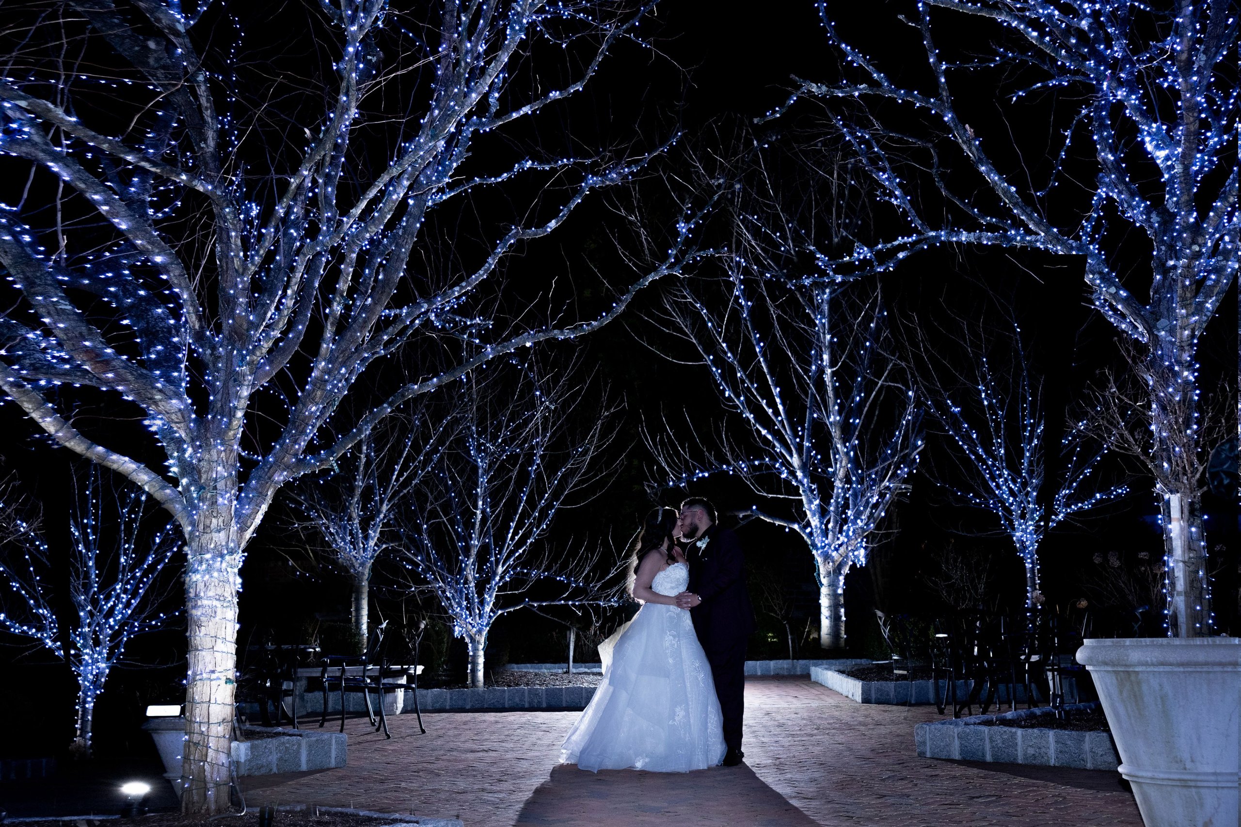 A bride and groom standing in front of a walkway lit up with blue lights.