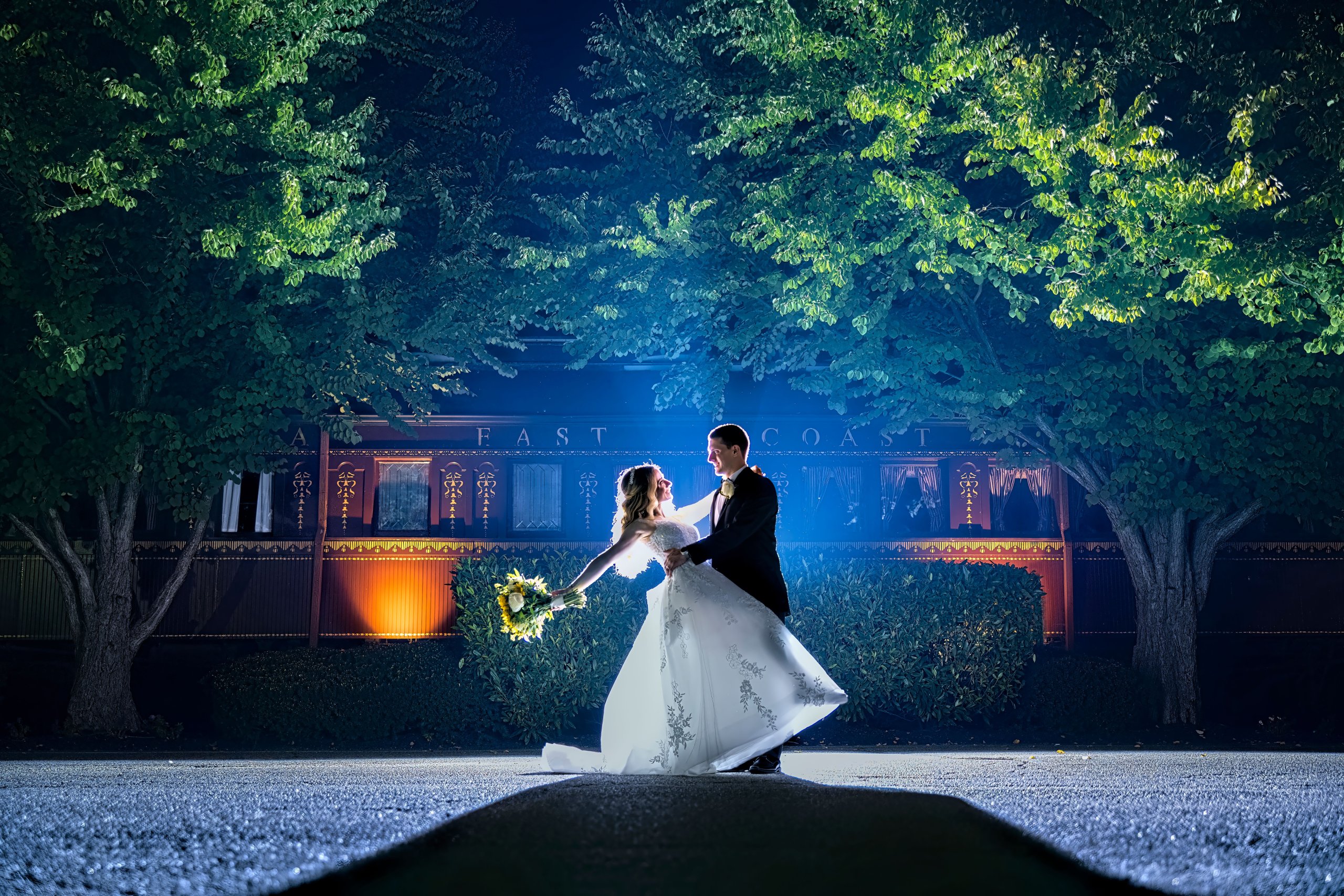 A bride and groom standing in front of trees at night.