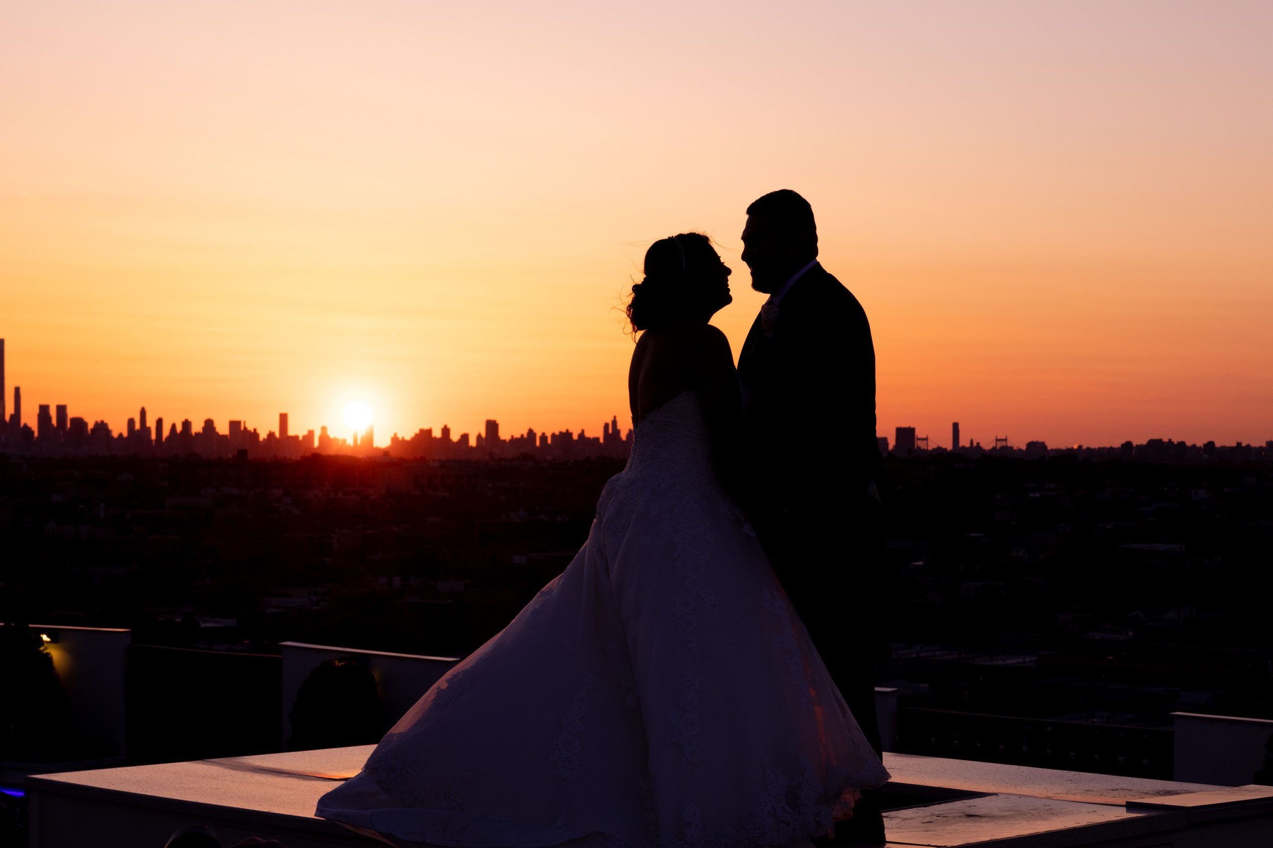 A bride and groom are silhouetted against the skyline at sunset.
