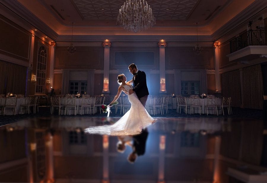 Bride and groom dance alone and do a dip on a dance floor with a light shining on them from behind