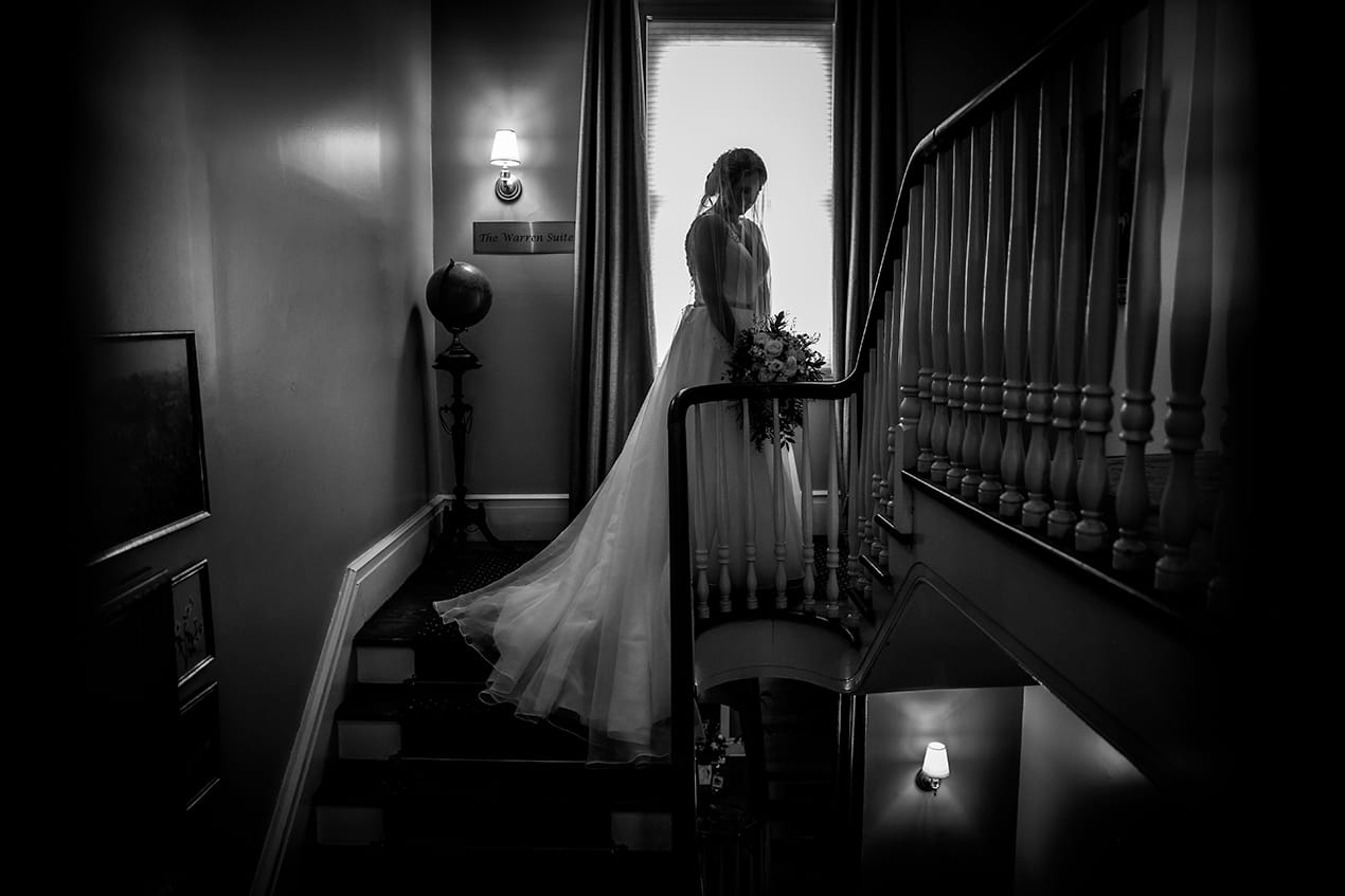 A bride is standing on a staircase in a black and white photo.